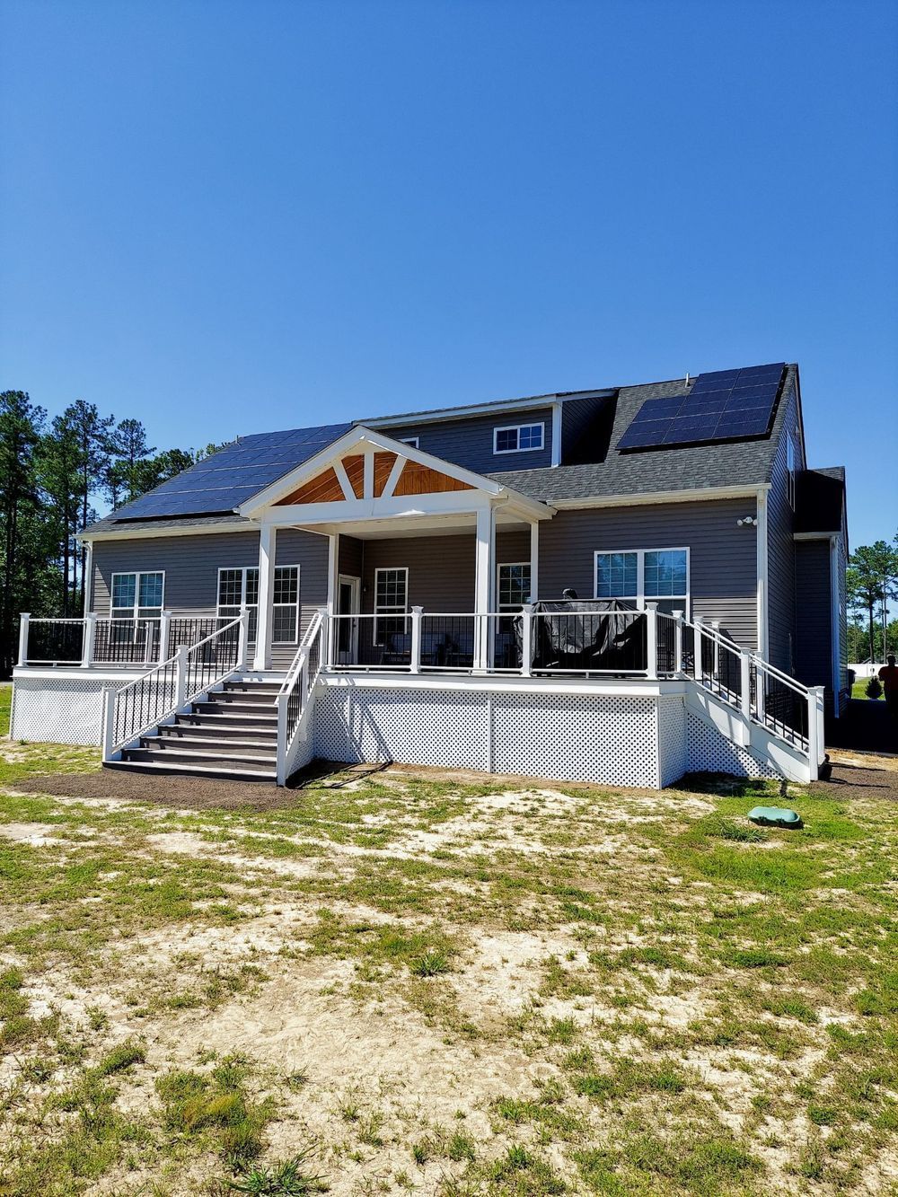 Two-story house with solar panels on roof, large deck, and clear blue sky.