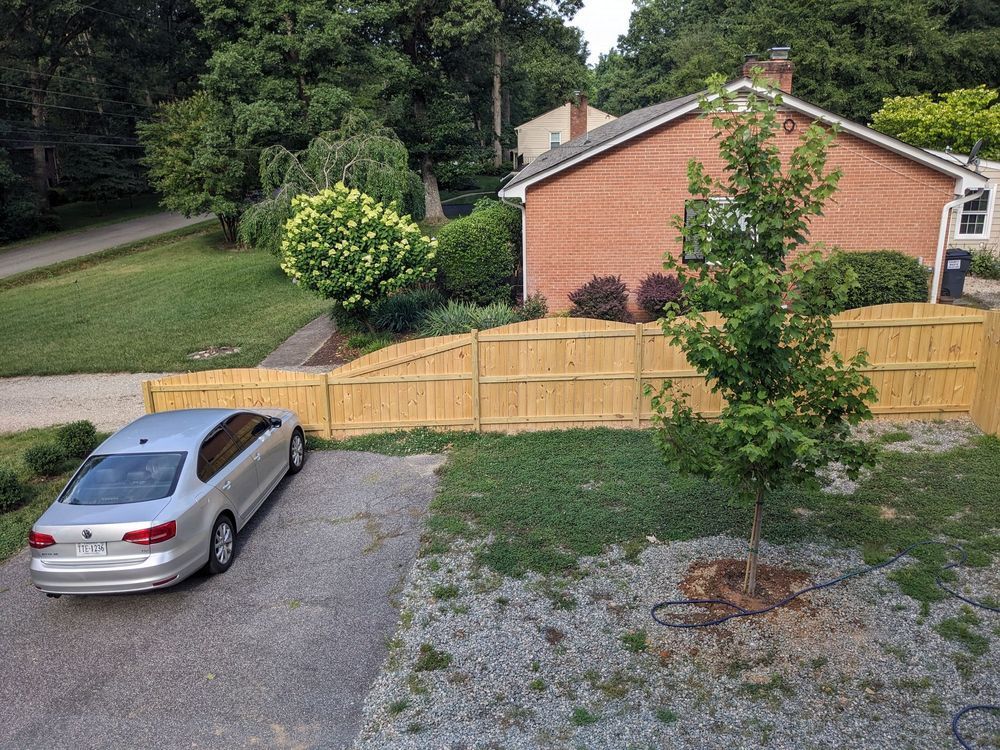 Silver car parked in a driveway next to a wooden fence. A brick house and trees are in the background.