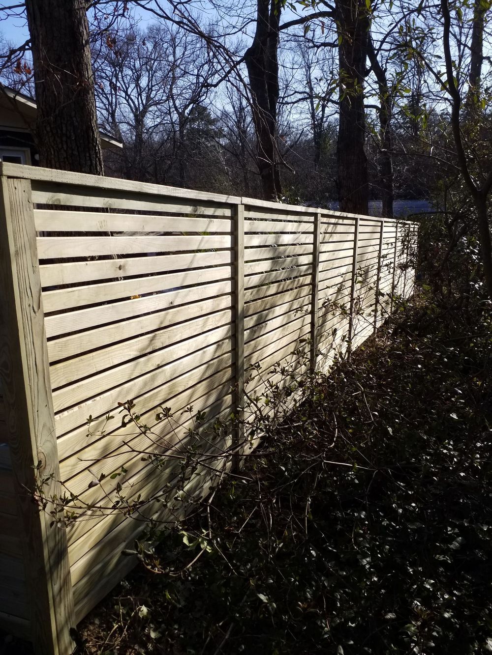 Wooden horizontal slat fence in a wooded area.