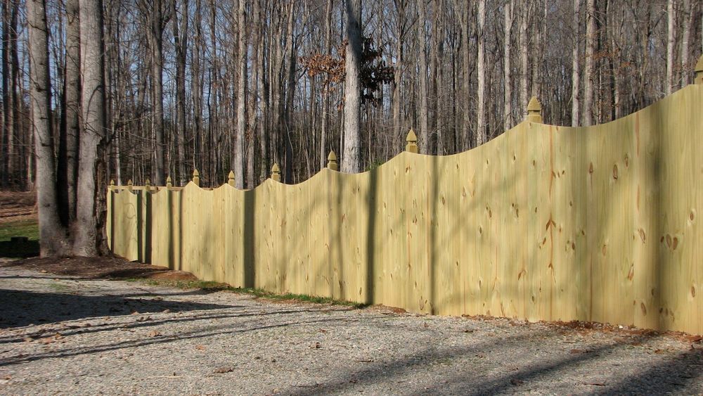Wooden fence with decorative finials along a gravel drive, with trees in the background.