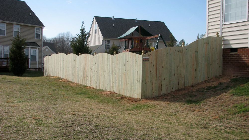 Wooden fence with scalloped top in a backyard.