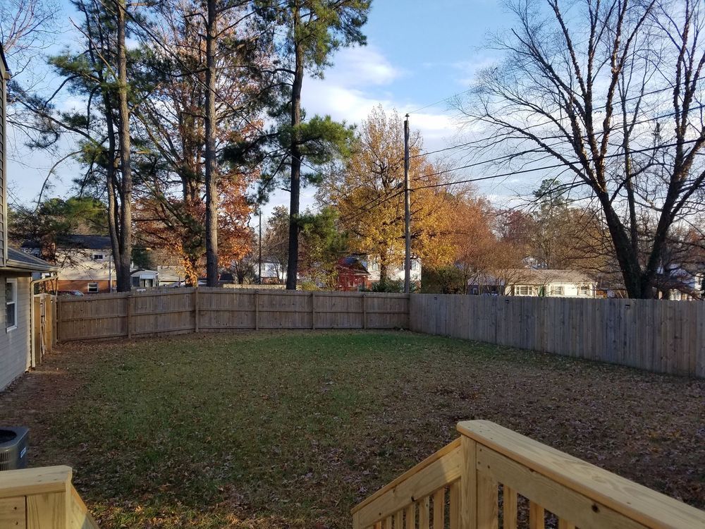 Backyard with wooden fence, grass, trees with fall foliage, and a clear blue sky.