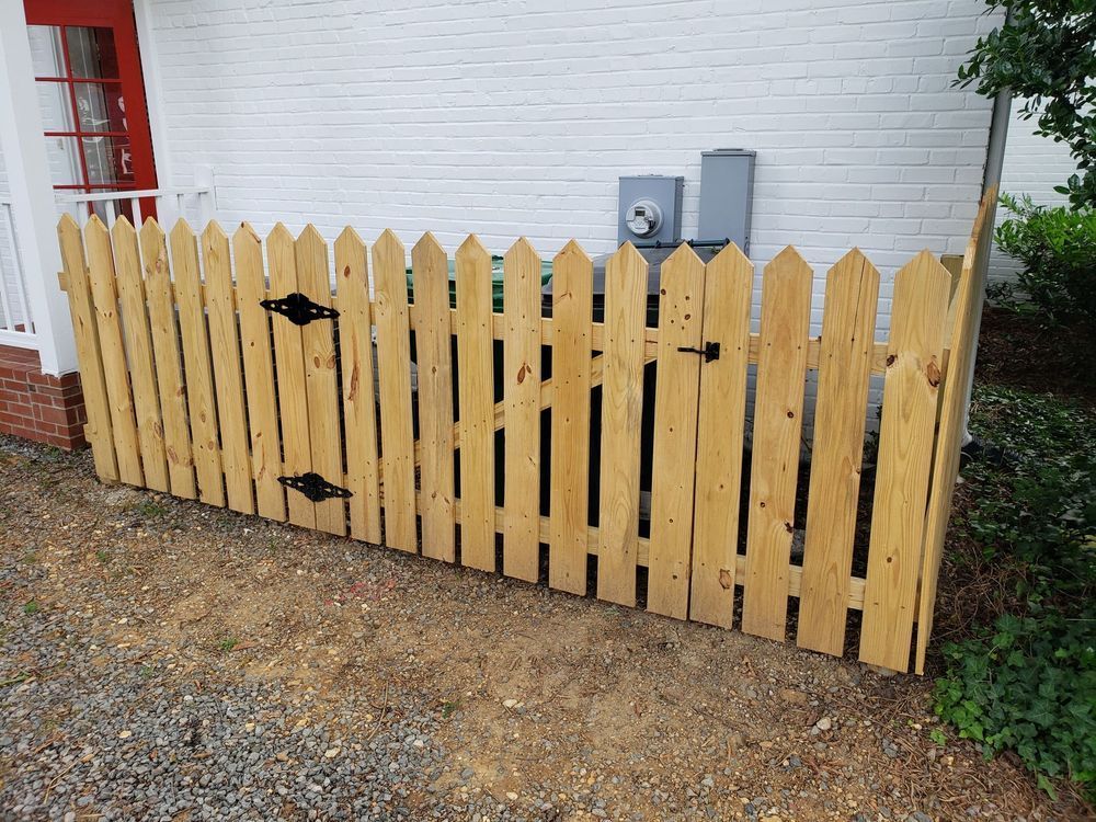 Wooden picket fence around electrical equipment against a white building.