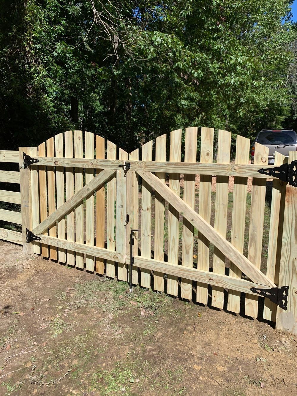 Wooden gate with curved top, attached to a wooden fence. Light green wood; black hardware. Outdoors.