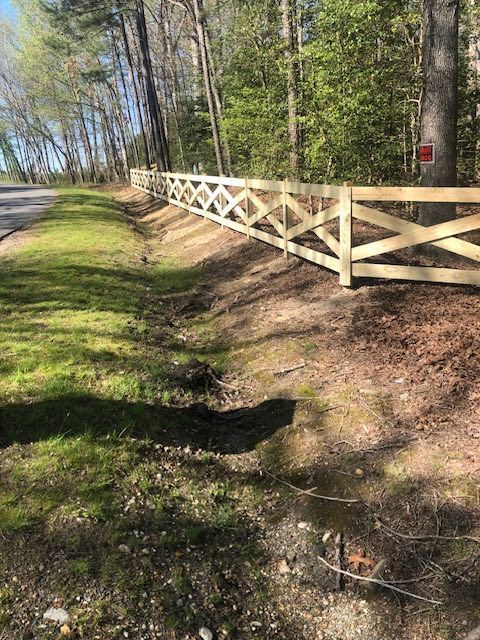 Wooden lattice fence along a roadside ditch in a wooded area.