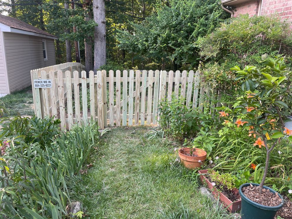 A small, wooden picket fence encloses a garden area with various plants and flowers; next to a shed.