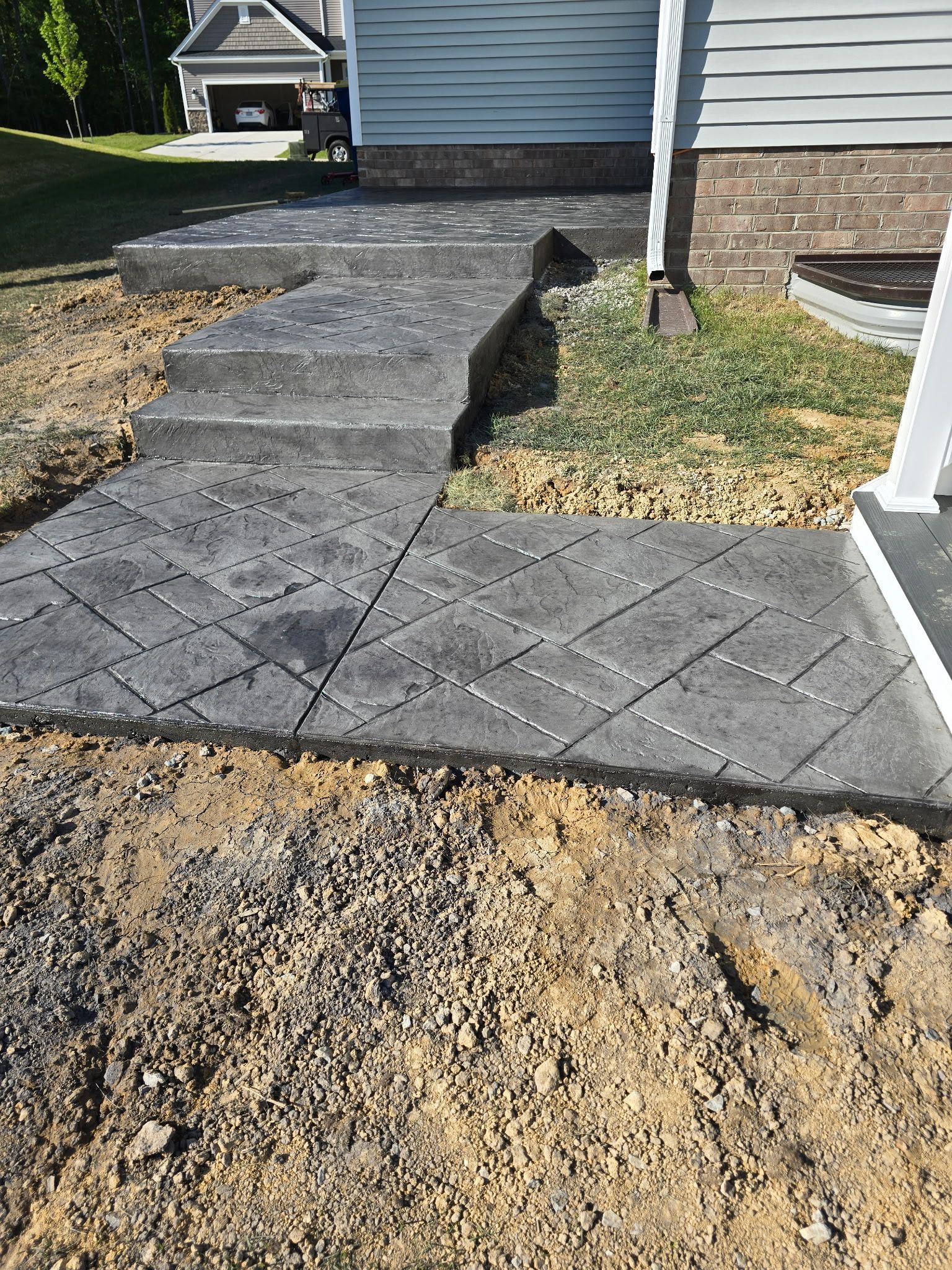 Front walkway under construction beside a house, with new concrete pavers and exposed dirt.
