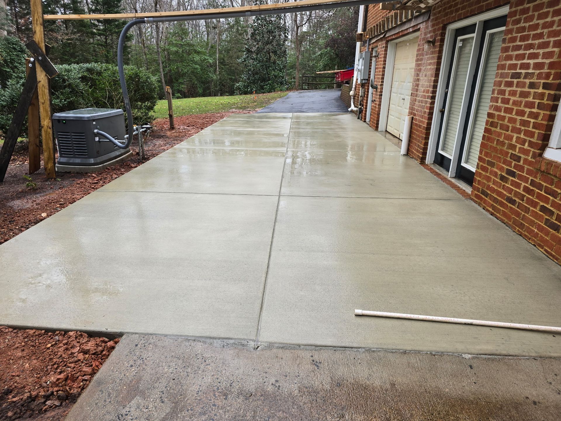 Wet concrete driveway beside a brick house with a garage and side yard fencing.