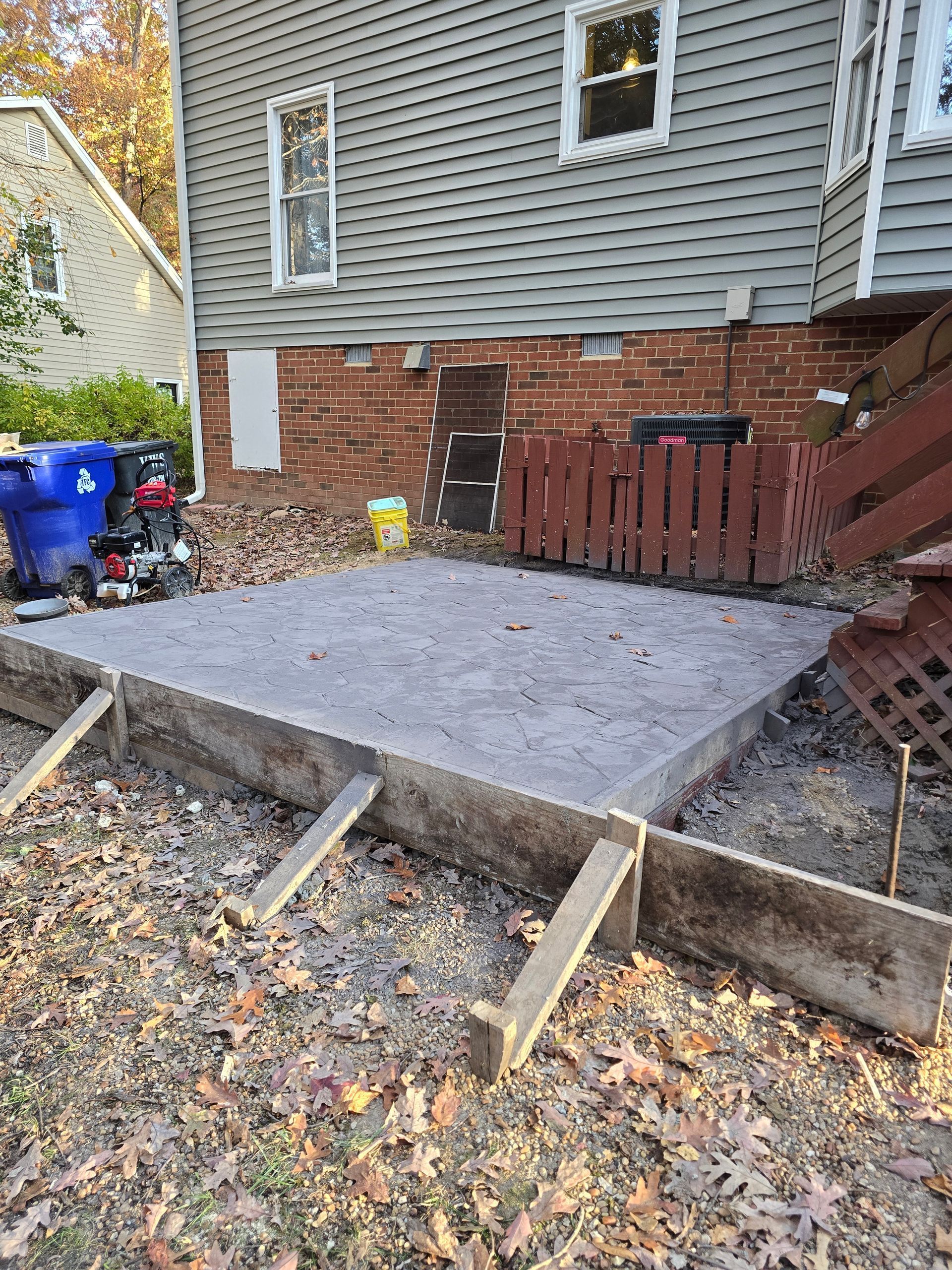 Fresh concrete patio slab beside a house with brick foundation and wooden framing forms in a backyard