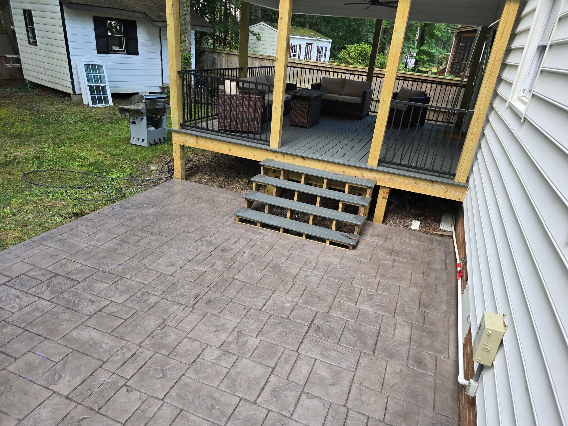 Brick patio with steps leading to a screened porch beside a white house and grassy yard