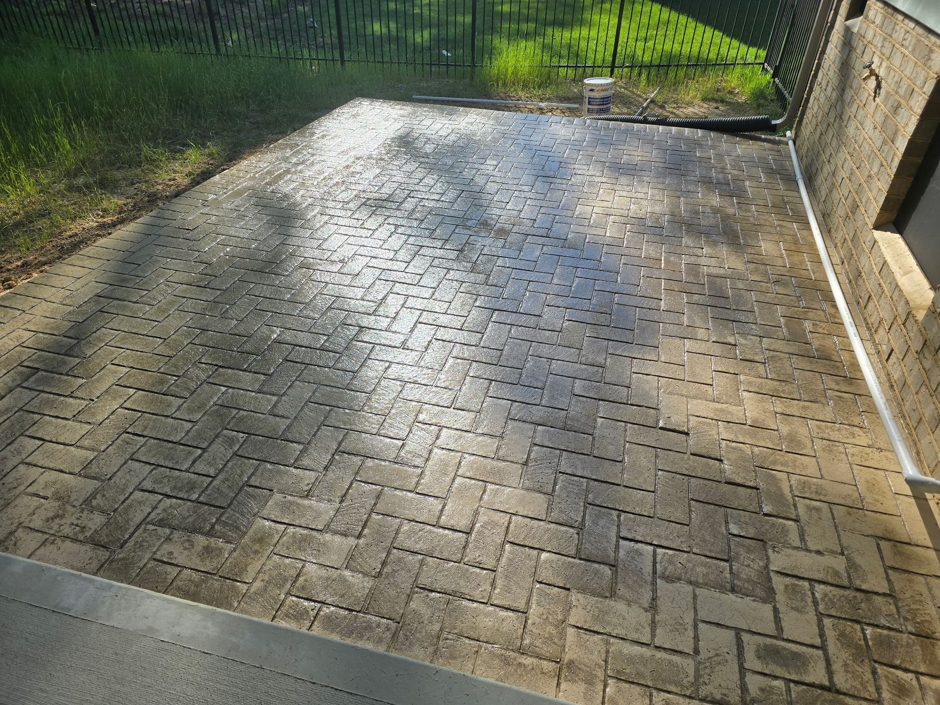Sunlit brick-paved patio beside a house, with a grass yard and fence beyond