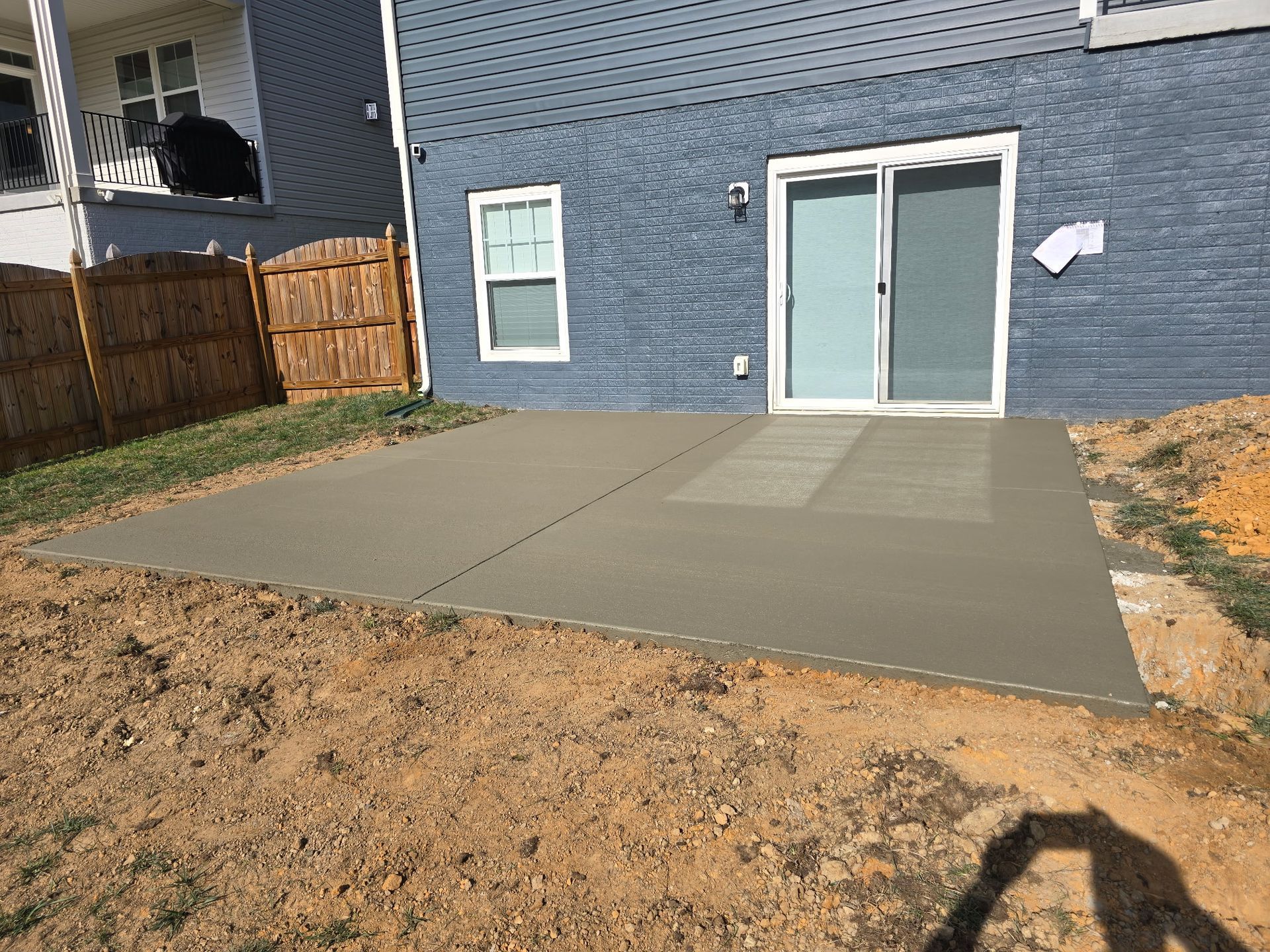Backyard concrete patio slab beside a blue house with sliding glass doors and a small window.