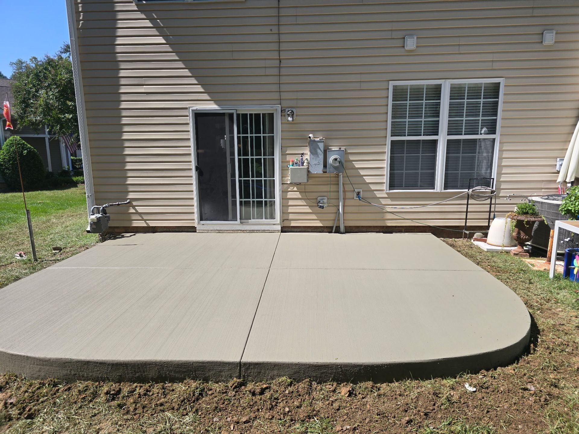 Concrete patio behind a house with a sliding glass door, window, and outdoor utility meters