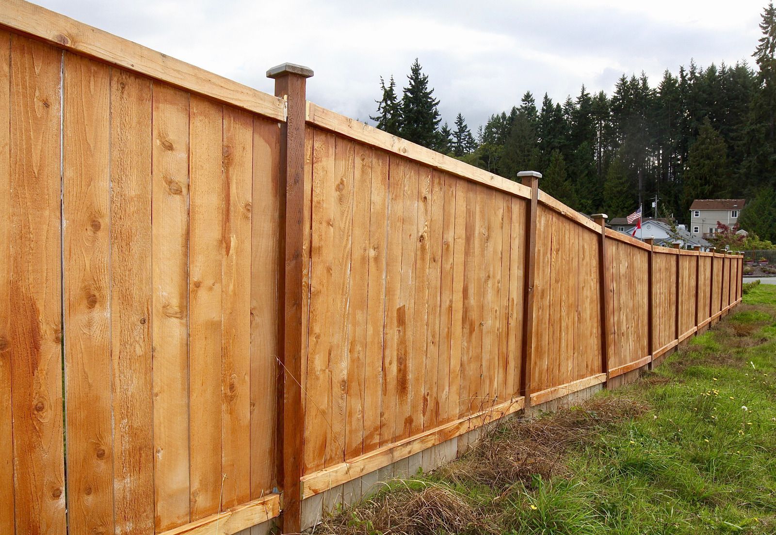 Wooden fence along a grassy edge, with trees in the background under an overcast sky.
