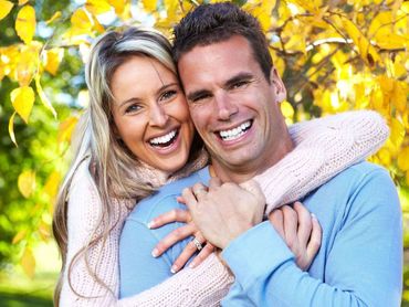 Learn More About Crowns & Bridges Services Smiling couple embracing outdoors with yellow foliage