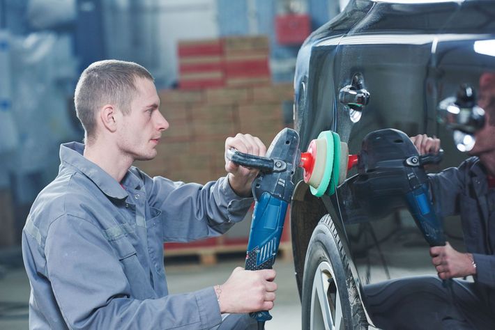 A man is polishing a car with a machine in a garage.