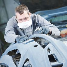 a man wearing a mask is working on a car .