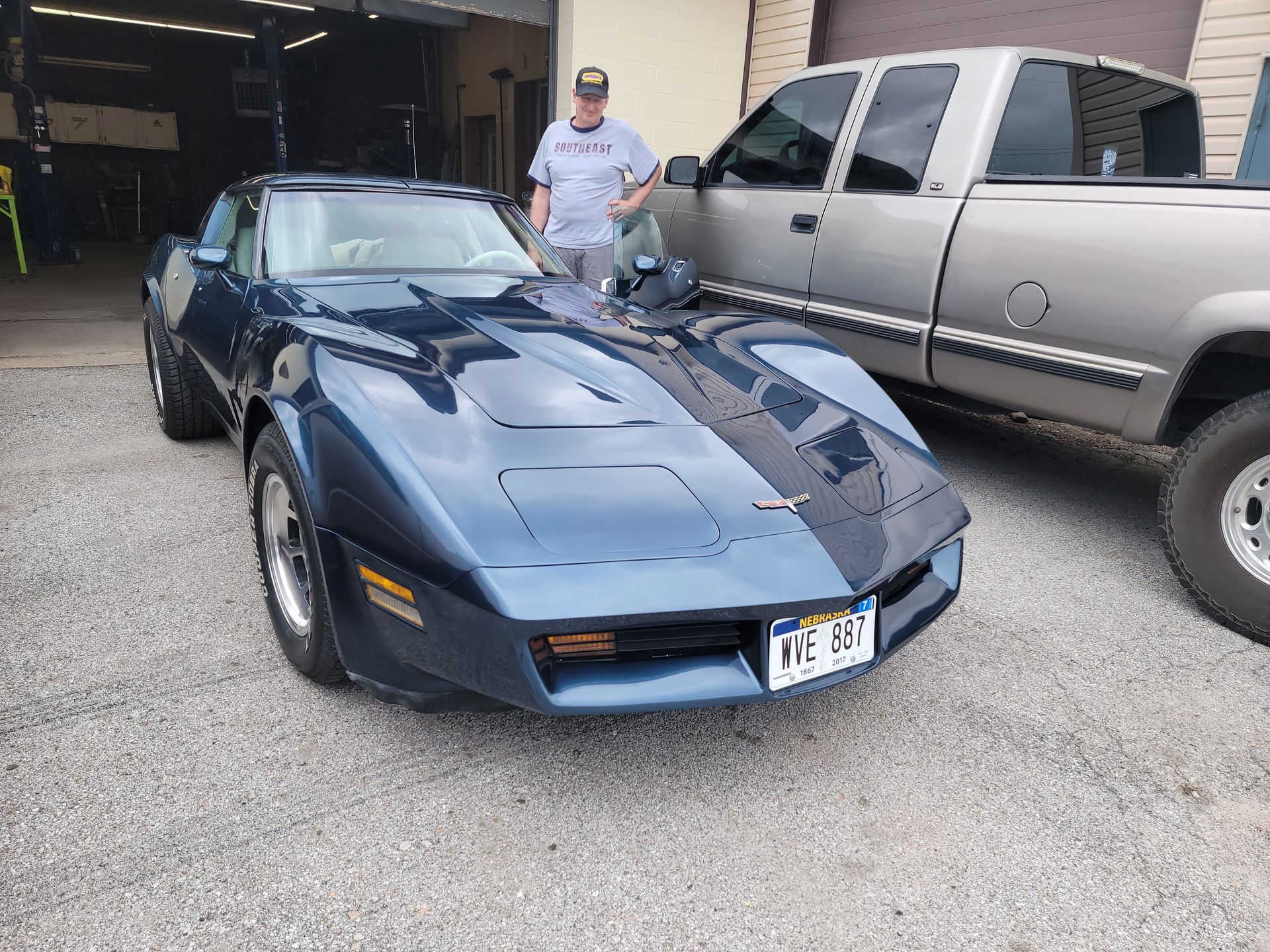 a man is standing next to a blue corvette and a silver truck
