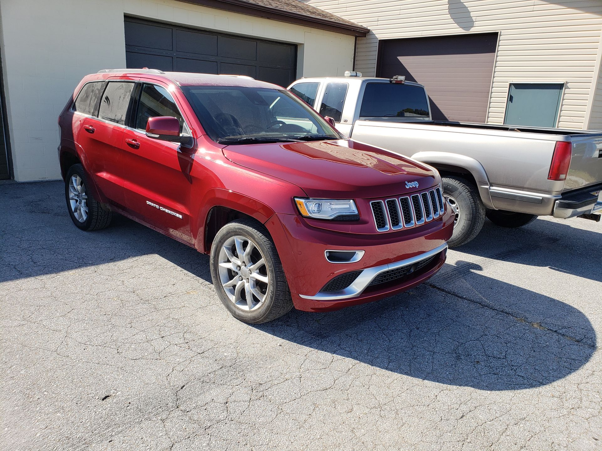 a red jeep grand cherokee is parked in front of a garage next to a silver truck