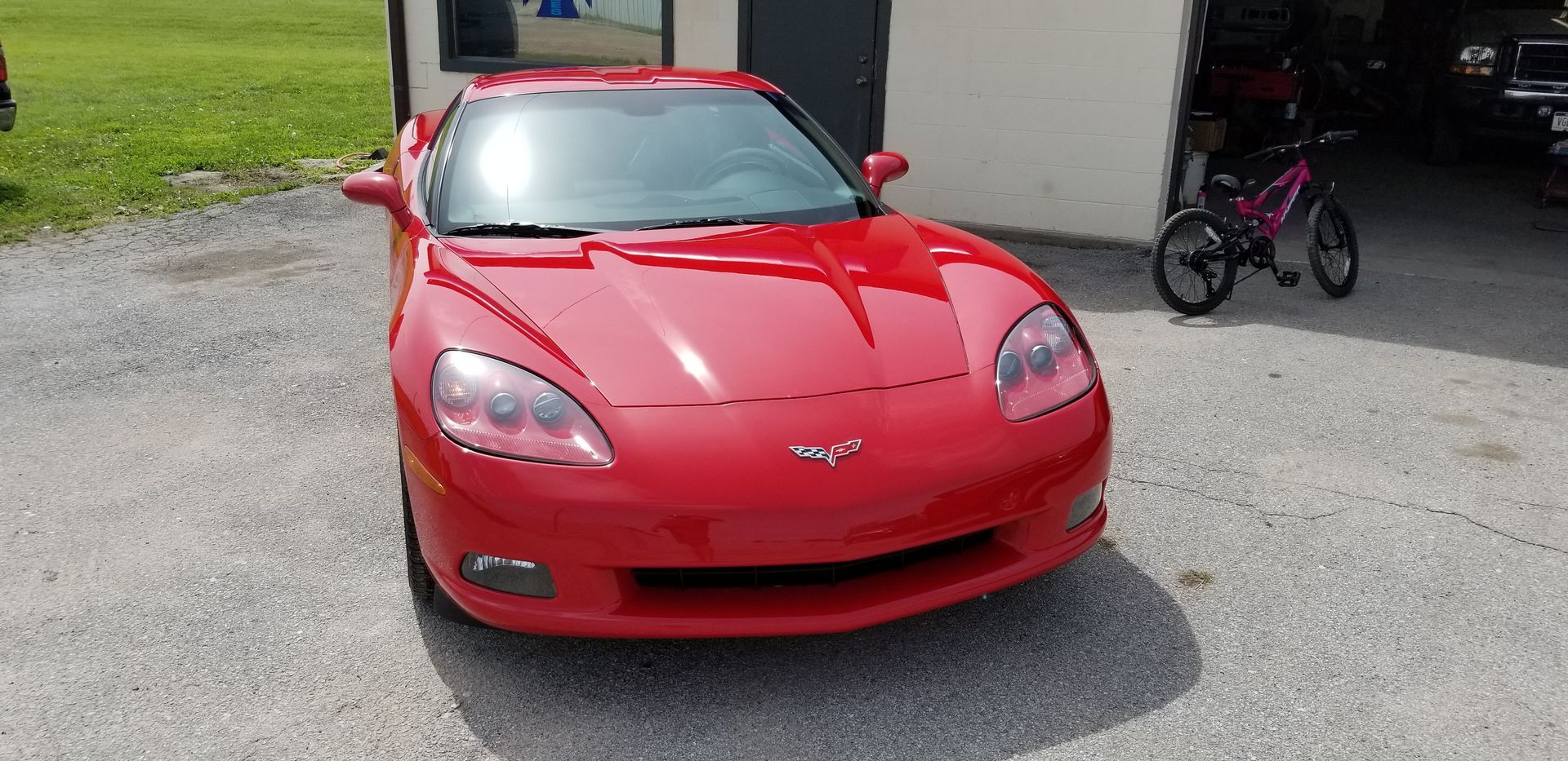 a red corvette is parked in a gravel lot in front of a garage