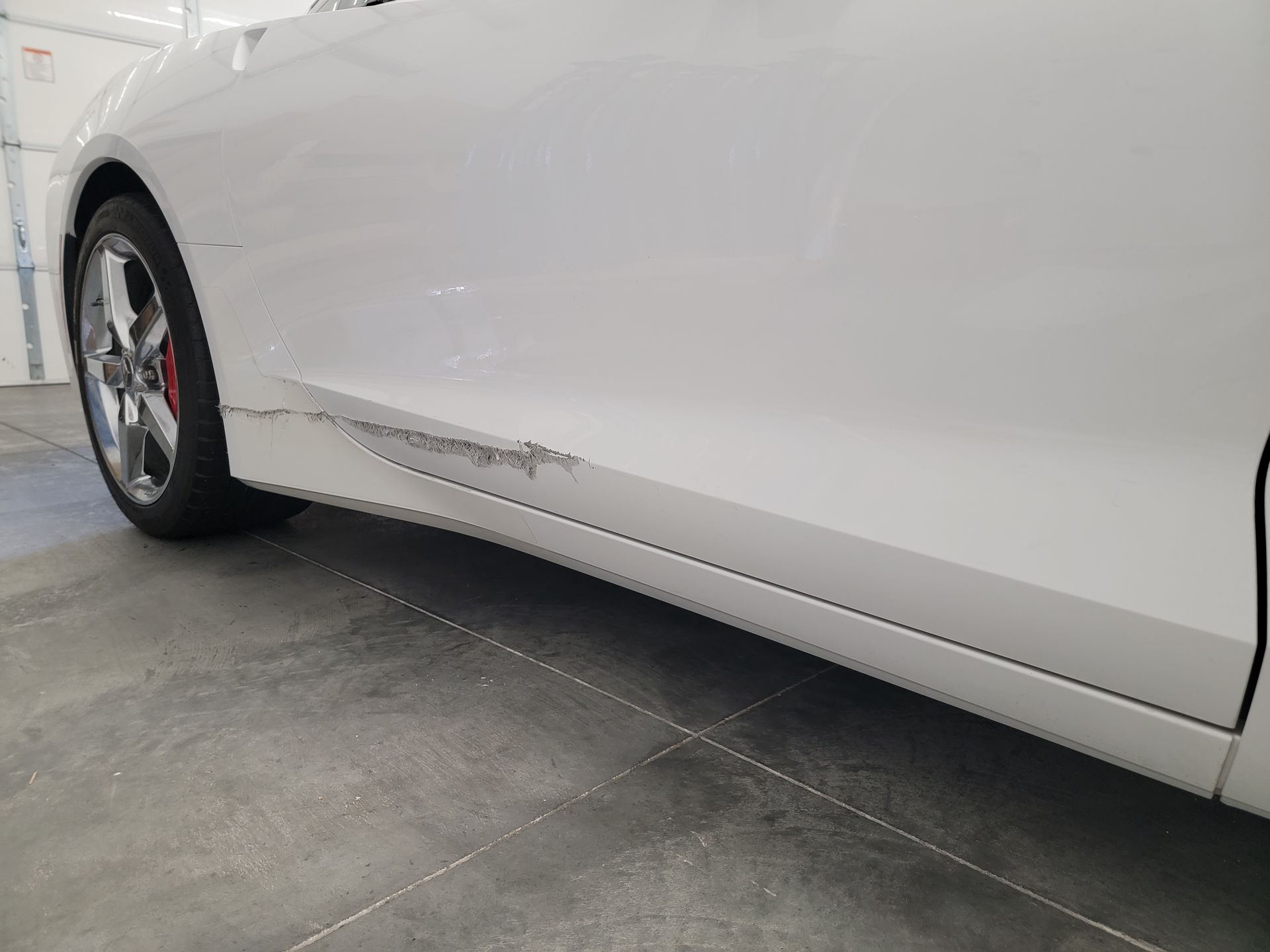 a white car with a damaged side door is parked in a garage