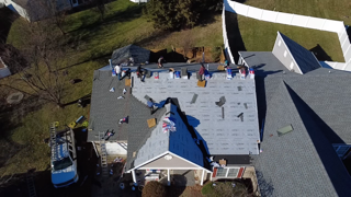 Roofers working on a residential roof, some applying shingles, materials spread out.
