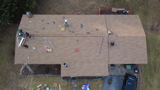 Overhead view of a roof with workers and materials scattered, suggesting roof repair in progress.