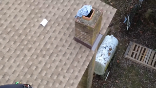 Brown shingle roof with a brick chimney, a water tank, and a wooden pallet next to it.