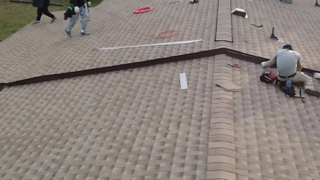 Roofers installing brown trim on a tan shingled roof; workers in the setting.