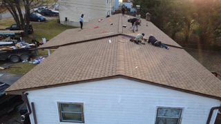 Workers installing shingles on a brown roof of a white house.