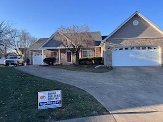 A residential home with a long driveway, a garage, and a sign for a roofing company on the lawn.