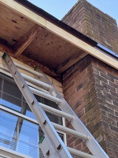 Ladder propped against a brick building, reaching toward damaged wooden eaves.
