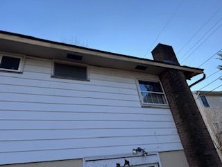 Side view of a white house with a brick chimney. Blue sky in the background.
