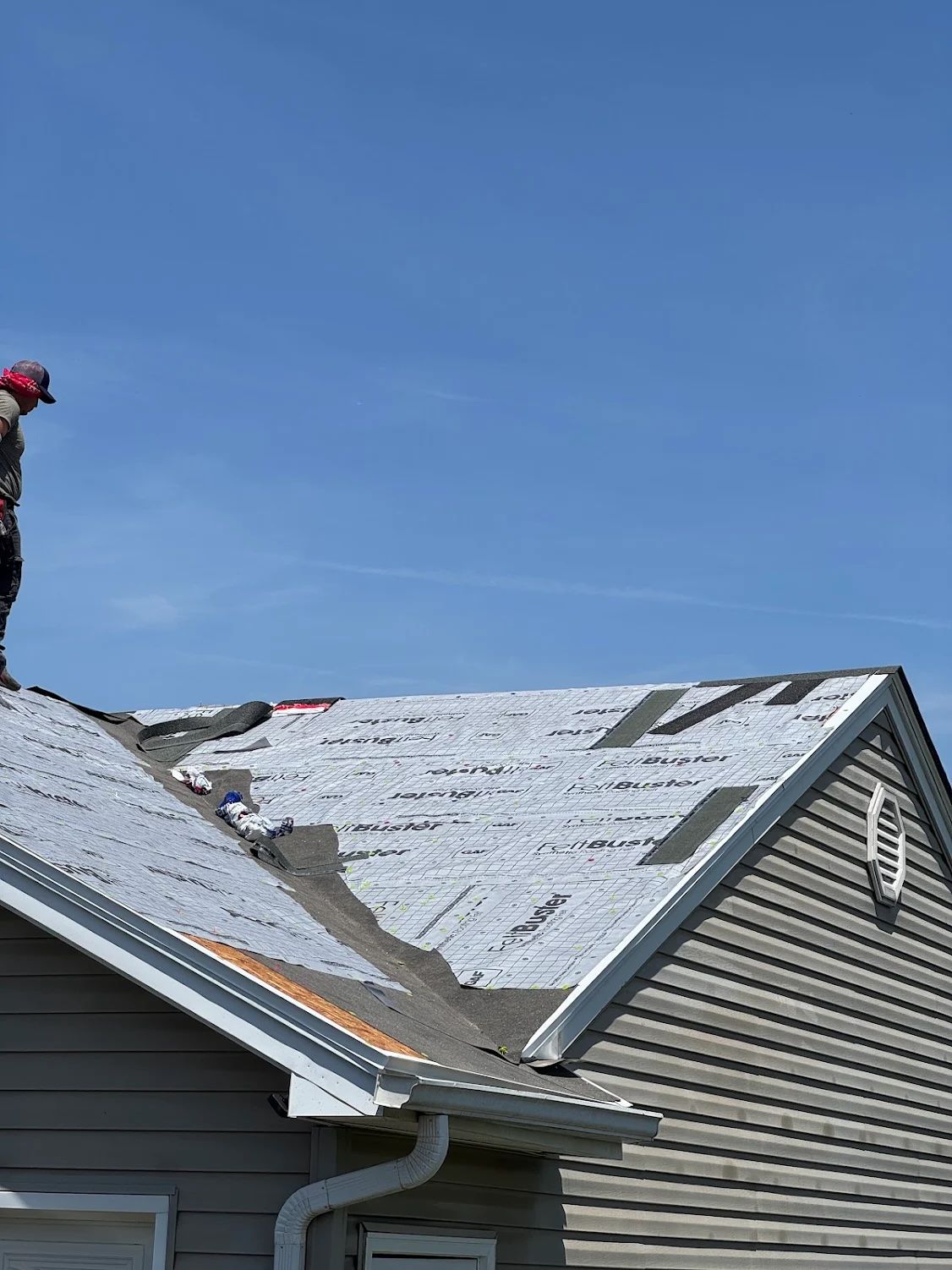 Person on a roof removing old shingles under a blue sky.