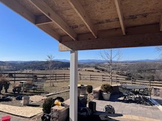 Construction of a covered patio with expansive mountain views, featuring lumber framing and blue sky.