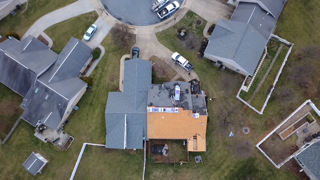 Aerial view of houses in a neighborhood, roofing work in progress. Cars and trucks are visible in driveways.