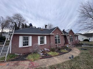 Roofers on a brick house, replacing shingles. Ladders, overcast sky.