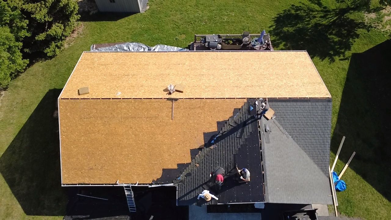 Roofers installing new shingles on a house roof; some sections complete, other areas uncovered.
