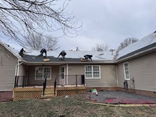 Roofers working on a residential roof, with a deck and backyard visible. Cloudy sky.