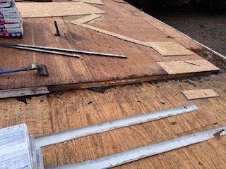 Roof being repaired, showing exposed wood, tools, and replacement boards.