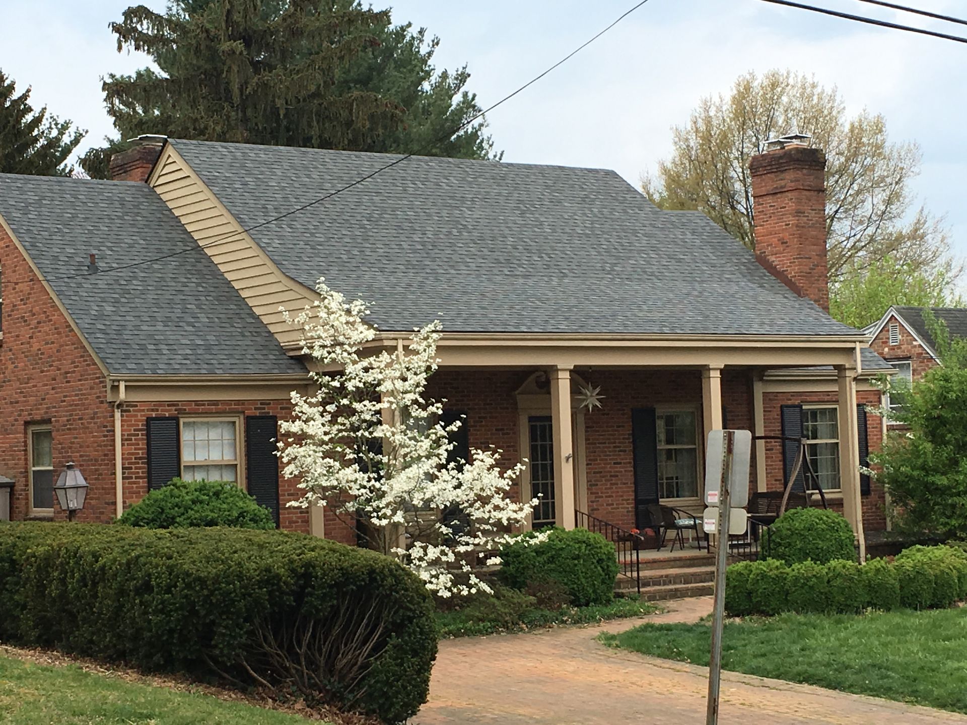 Brick house with a porch, black shutters, and a flowering dogwood tree; a sidewalk leads to the entrance.
