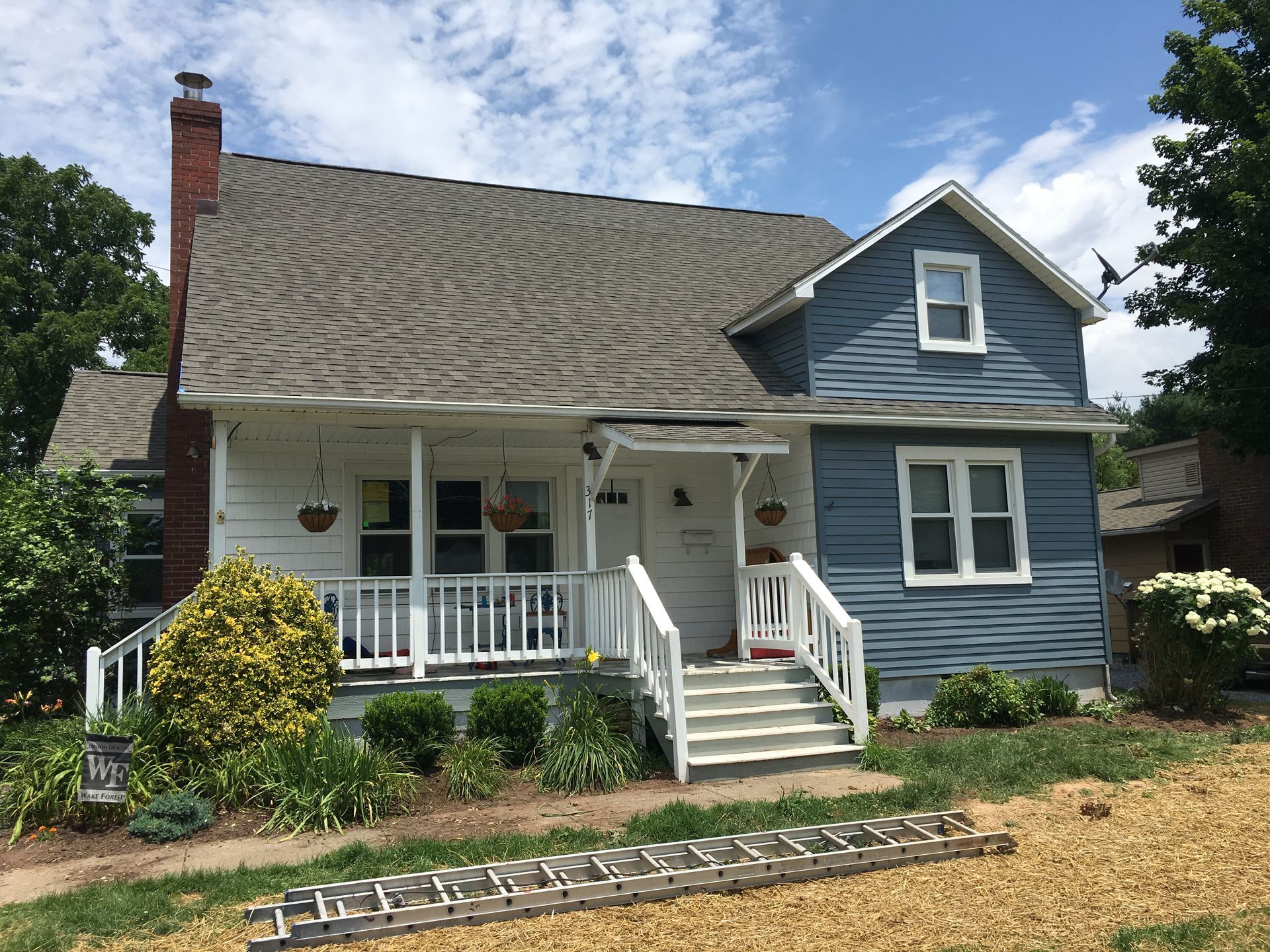 White and blue house with porch, chimney, and gray roof; ladder in front.