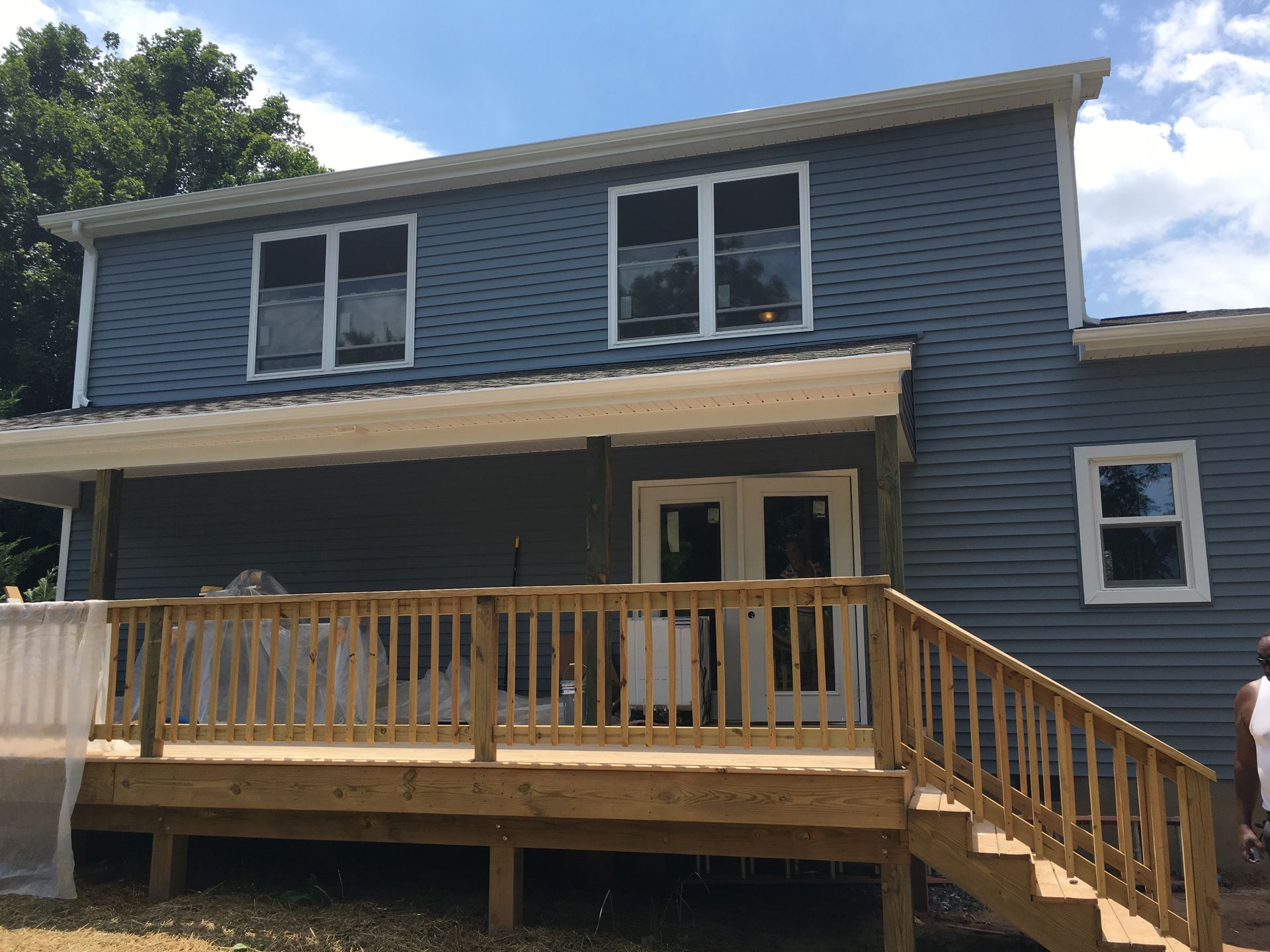 Back of a two-story blue house with wooden deck, steps, and double doors.