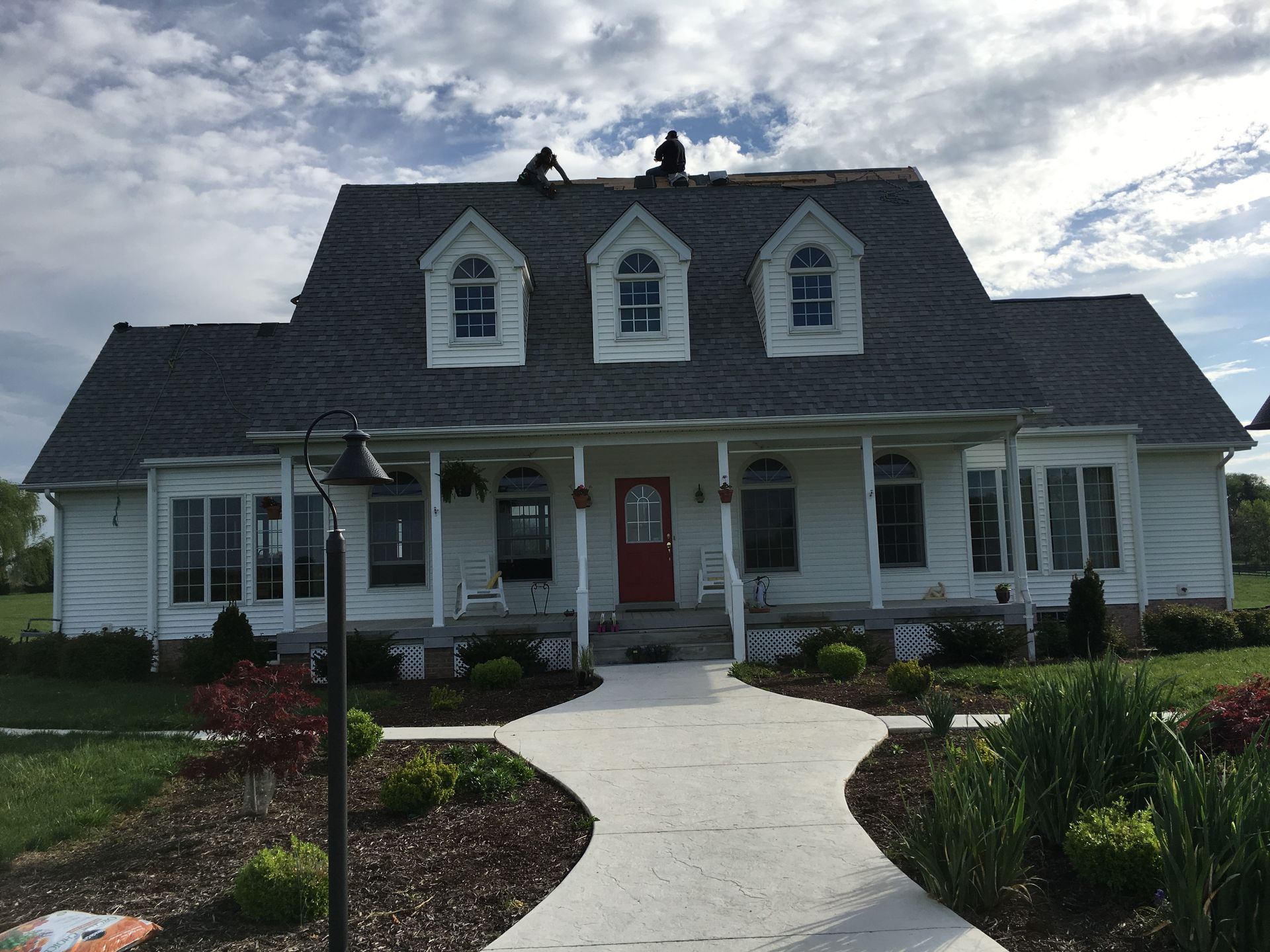 Workers on a two-story white house with a porch, replacing the roof. Sky in background.