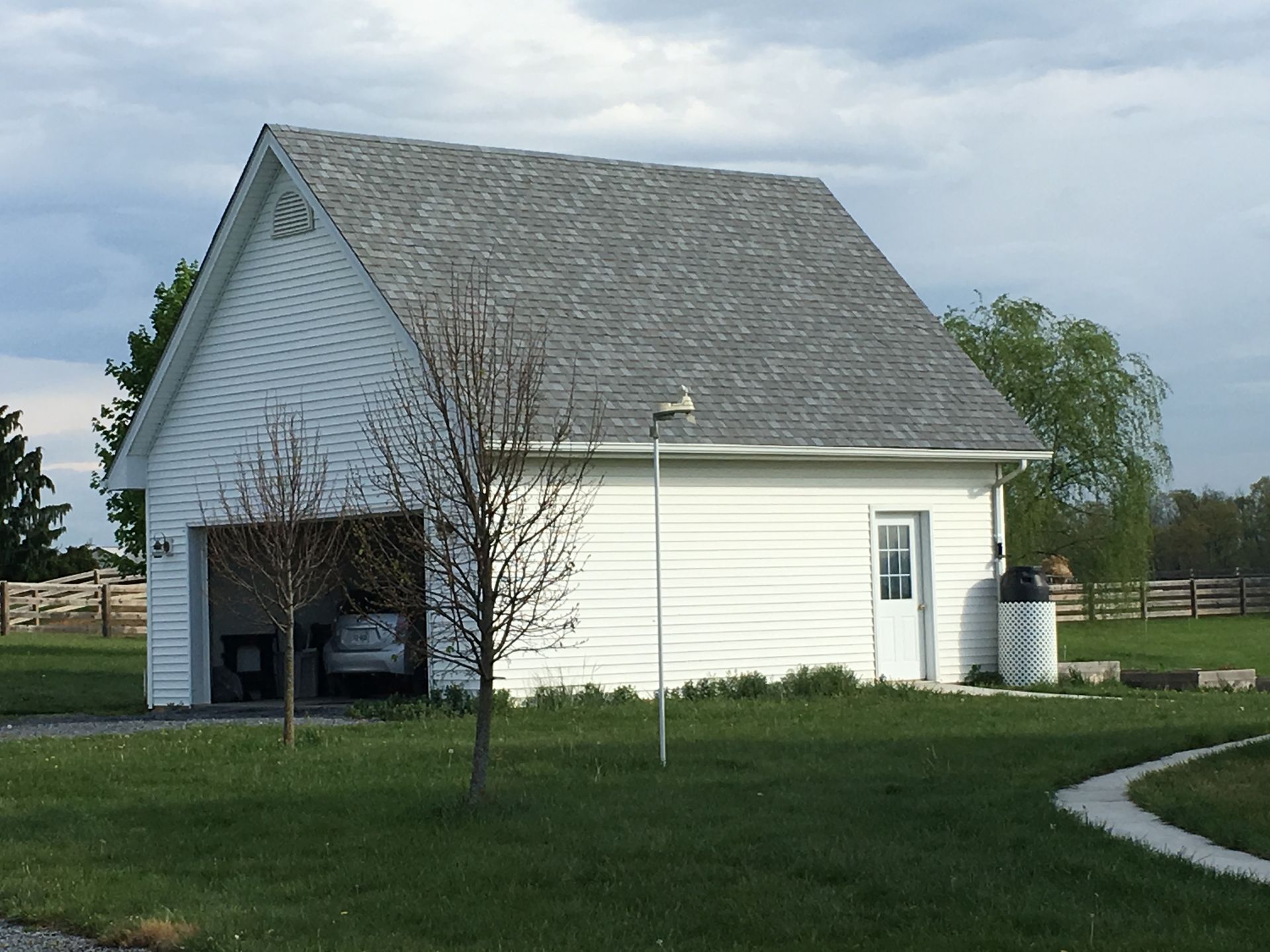 White two-story garage with gray roof, open door revealing a car, small door on side, on green grass.