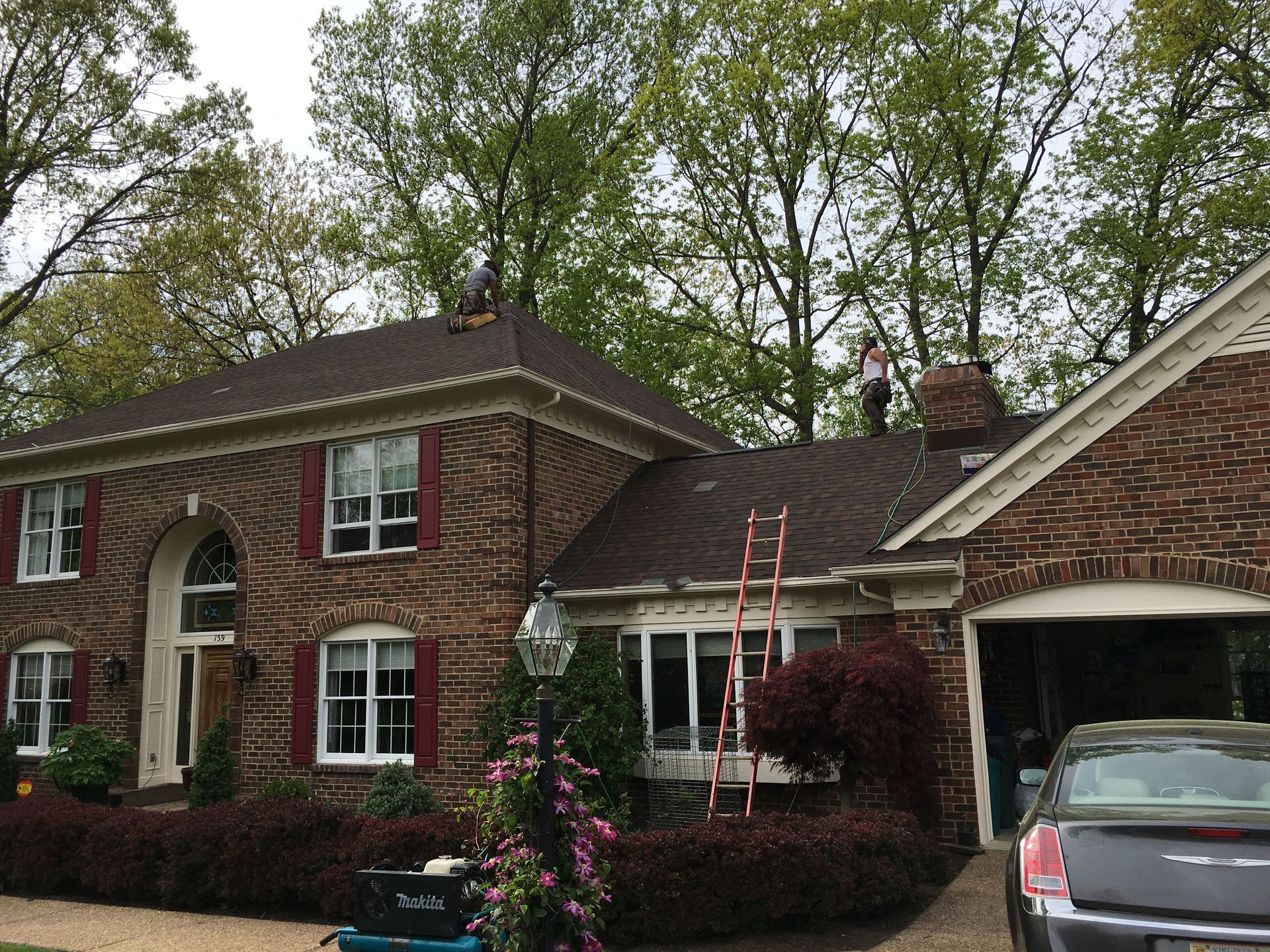 Roofers on a brick house roof with a ladder, cloudy sky.