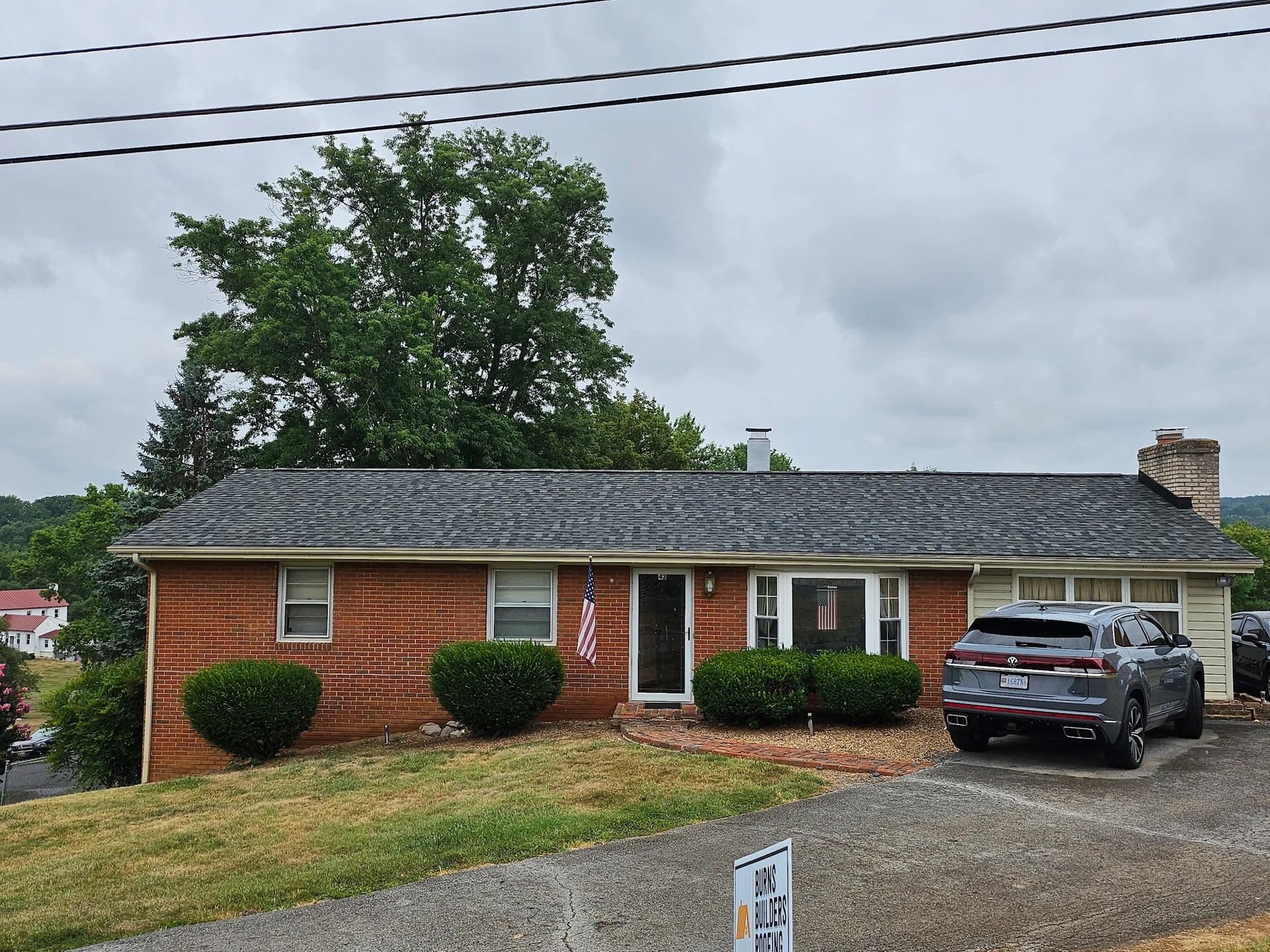 Brick ranch-style house on a slight hill with a car parked in the driveway; cloudy sky above.
