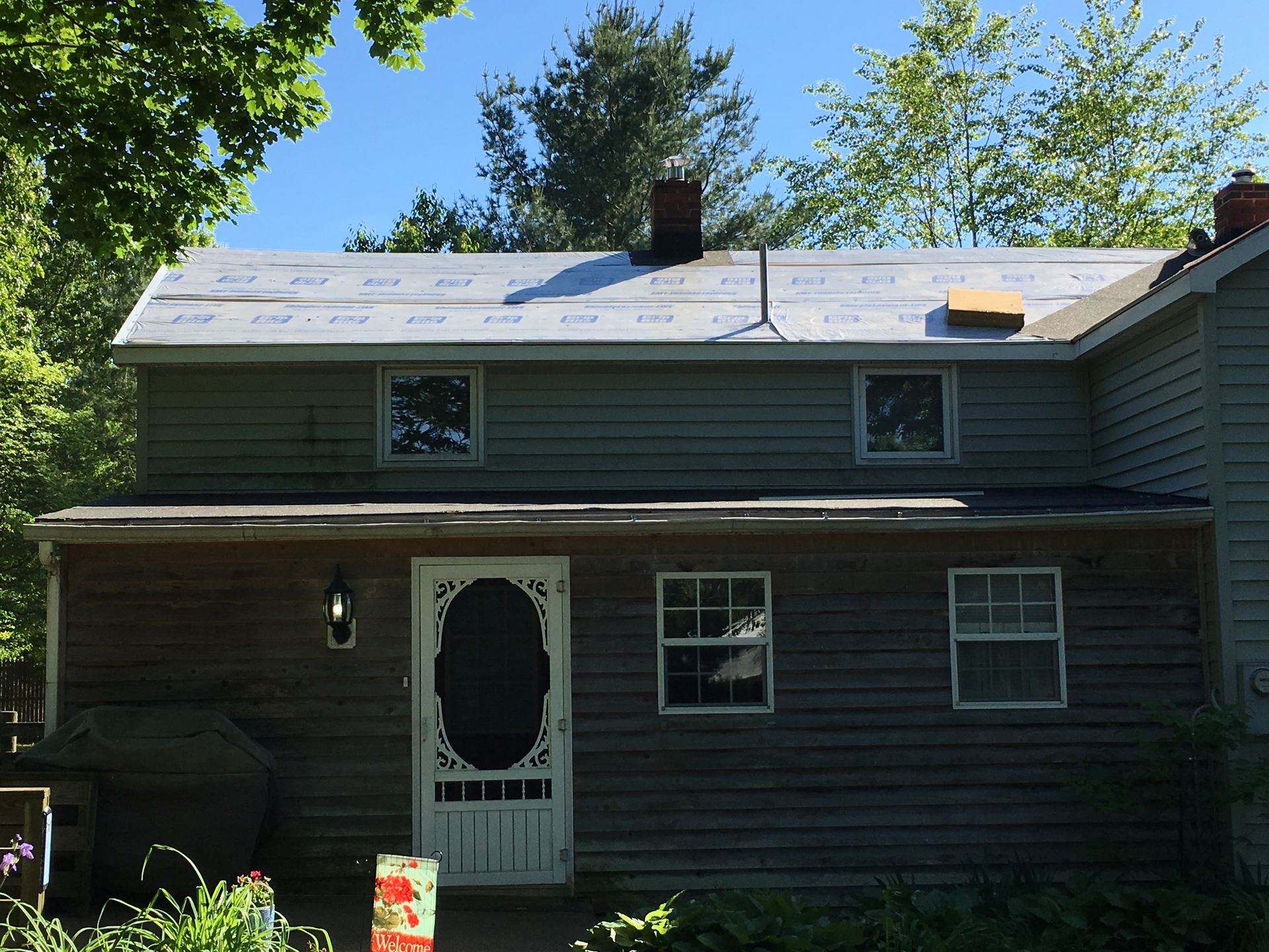 Two-story house with siding; roof partly missing. Front door with screen, windows, and chimney.