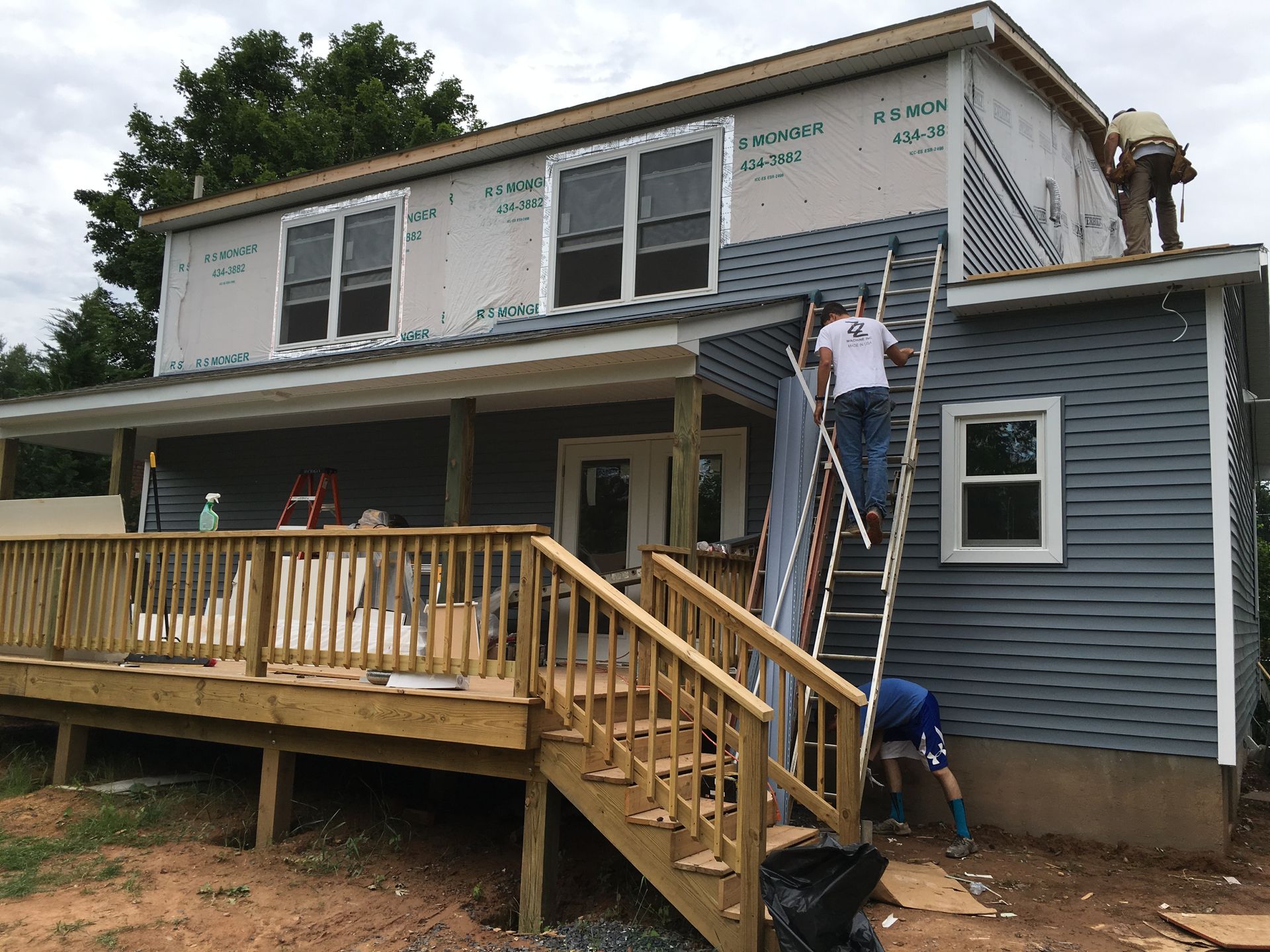 Construction workers building a two-story house with a wooden deck and blue siding.