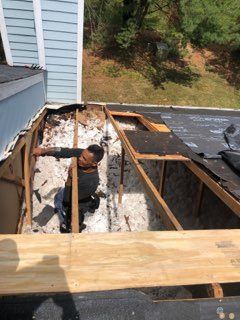 A person works on a roof with a damaged section and exposed framing.